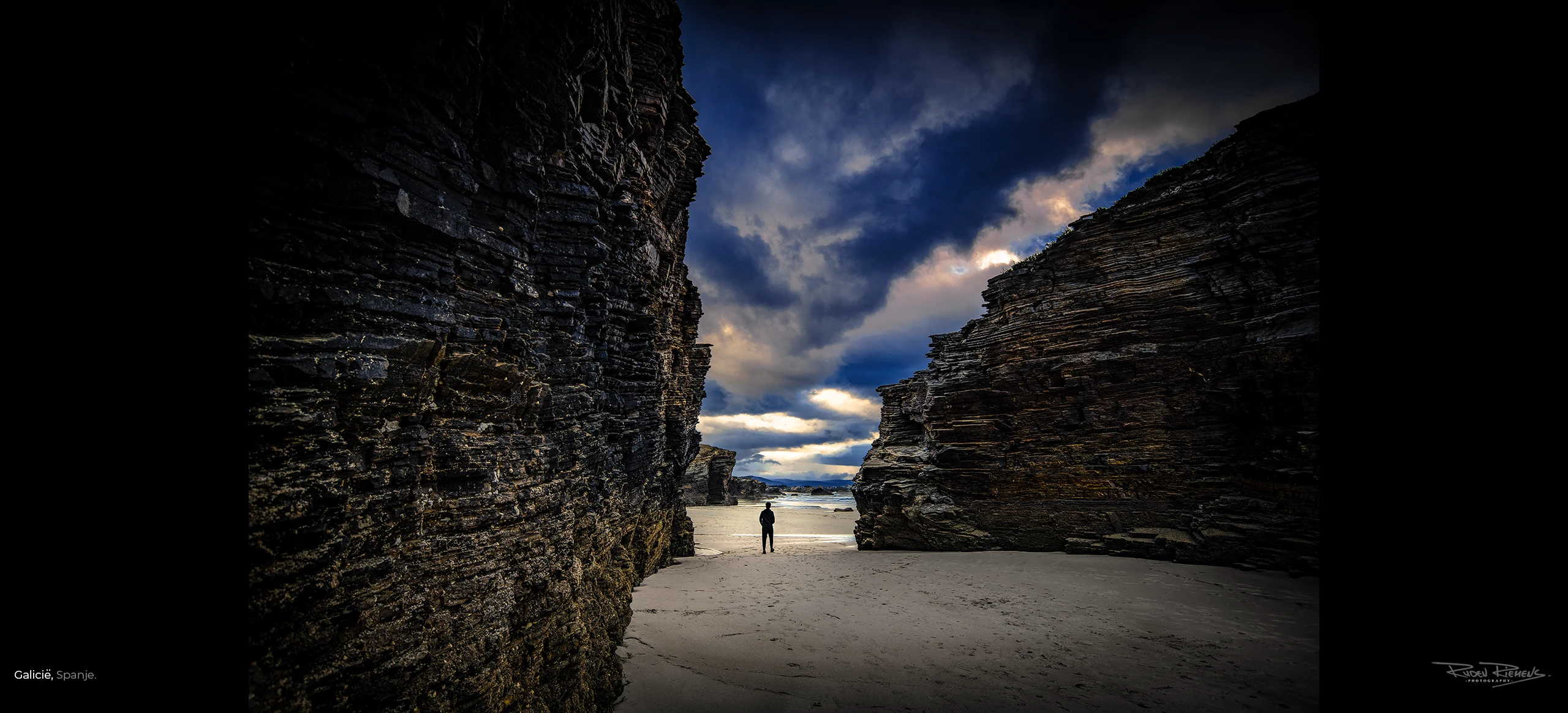 Foto van wandelaar op strand tussen de rotsen aan de kust van Galicië Spanje, door Ruden Riemens Photography.