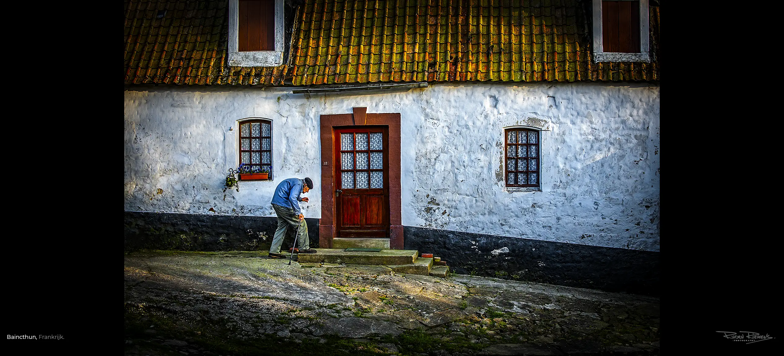 Bijna thuis, kromgebogen man met wandelstok arriveert bij zijn huis in Baincthun Frankrijk, Ruden Riemens Photography.