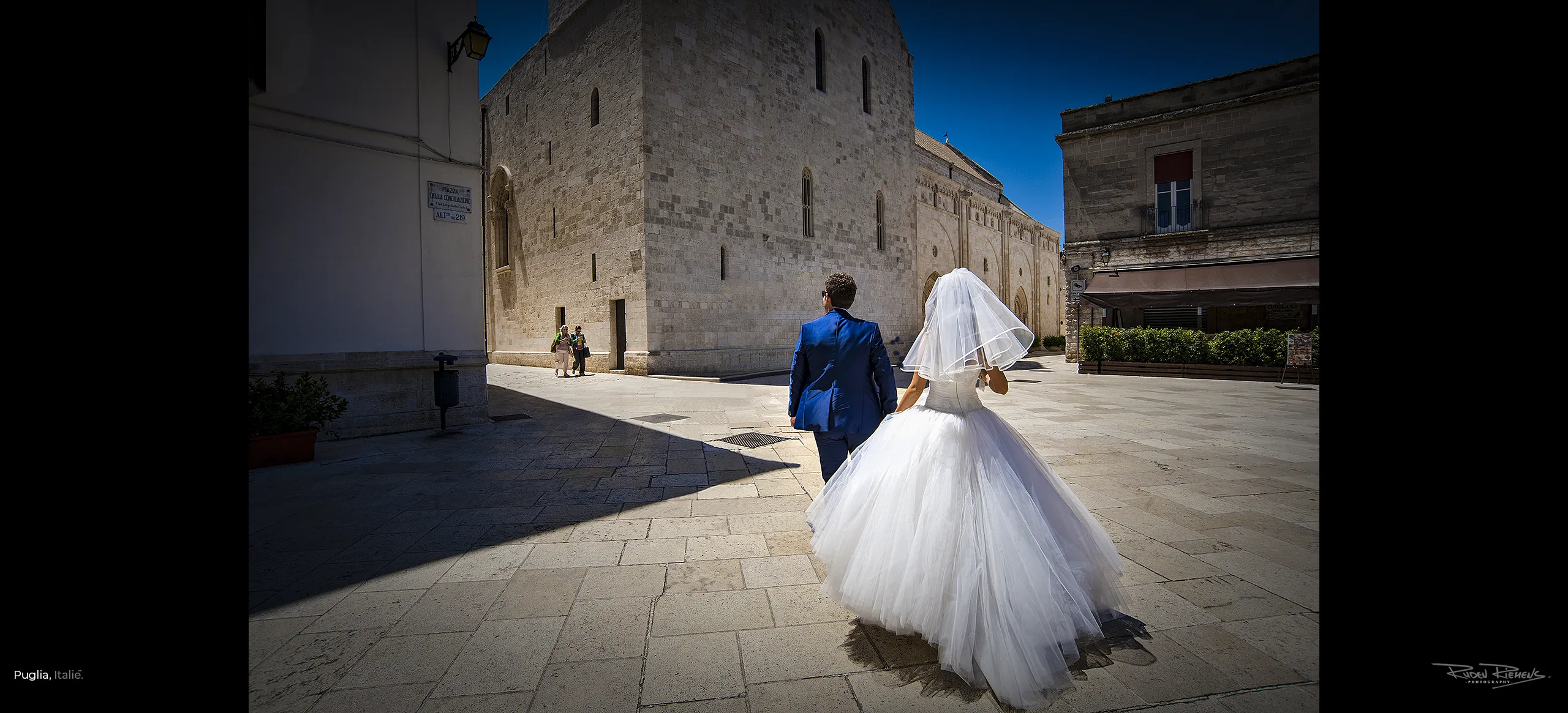 Bruidspaar op weg naar het altaar, straatfotografie in Puglia Italië, kunst aan de muur, foto van Ruden Riemens Fotograaf.