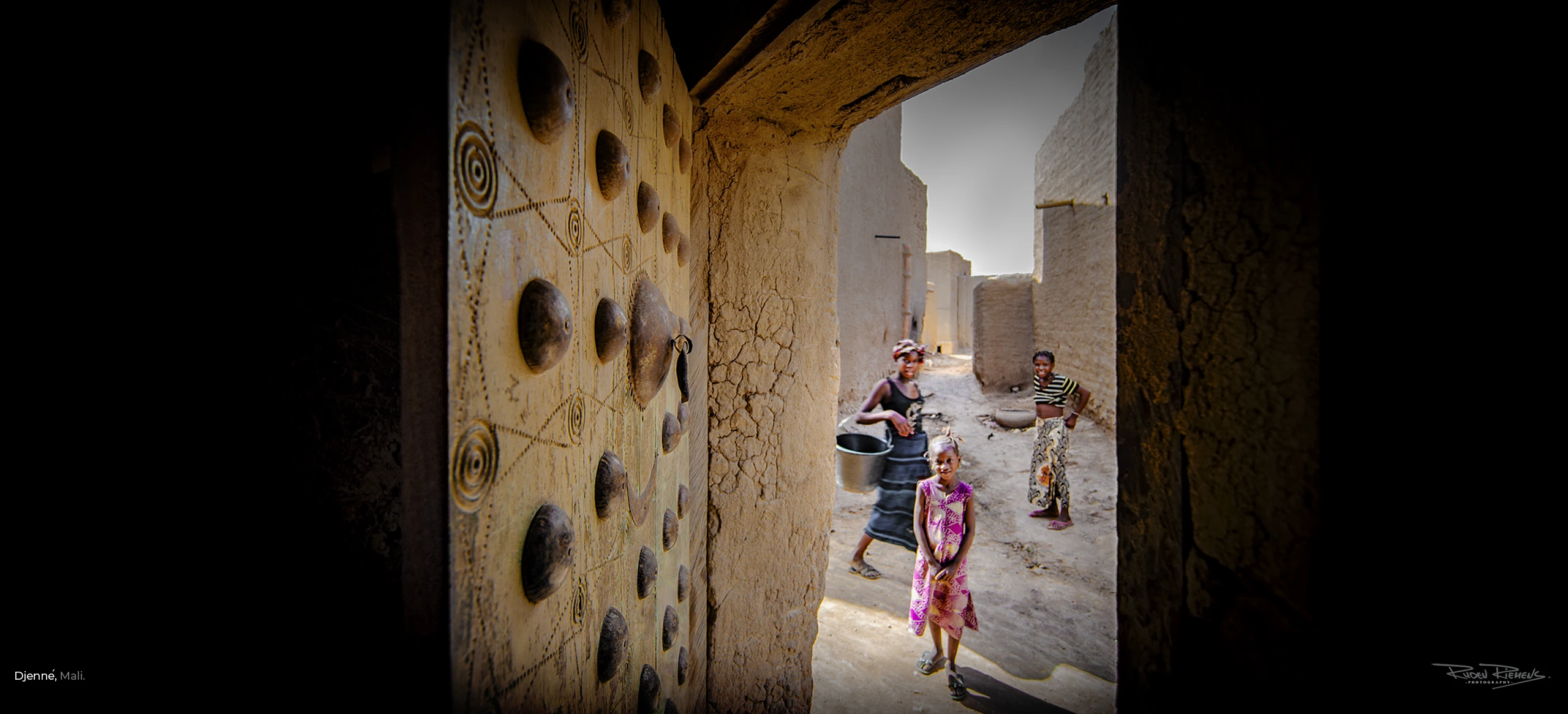 Straatbeeld met voorbijgangers door deuropening gefotografeerd in Djenné Mali, door Ruden Riemens Fotografie.