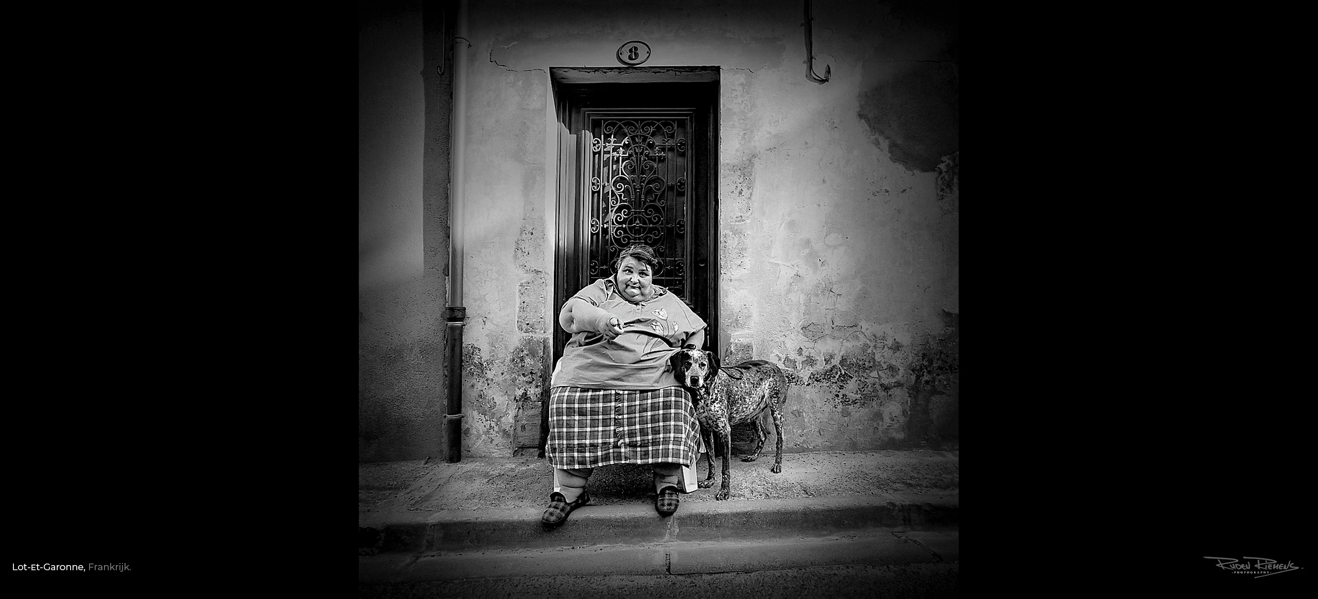 Portret van Ruden Riemens Fotograaf op reis van een corpulente vrouw op stoel met hond voor haar huis in de Lot-et-Garonne. Deze foto maakte deel uit van een serie portretten uit dit gebied, ooit genomineerd voor De Zilveren Camera.