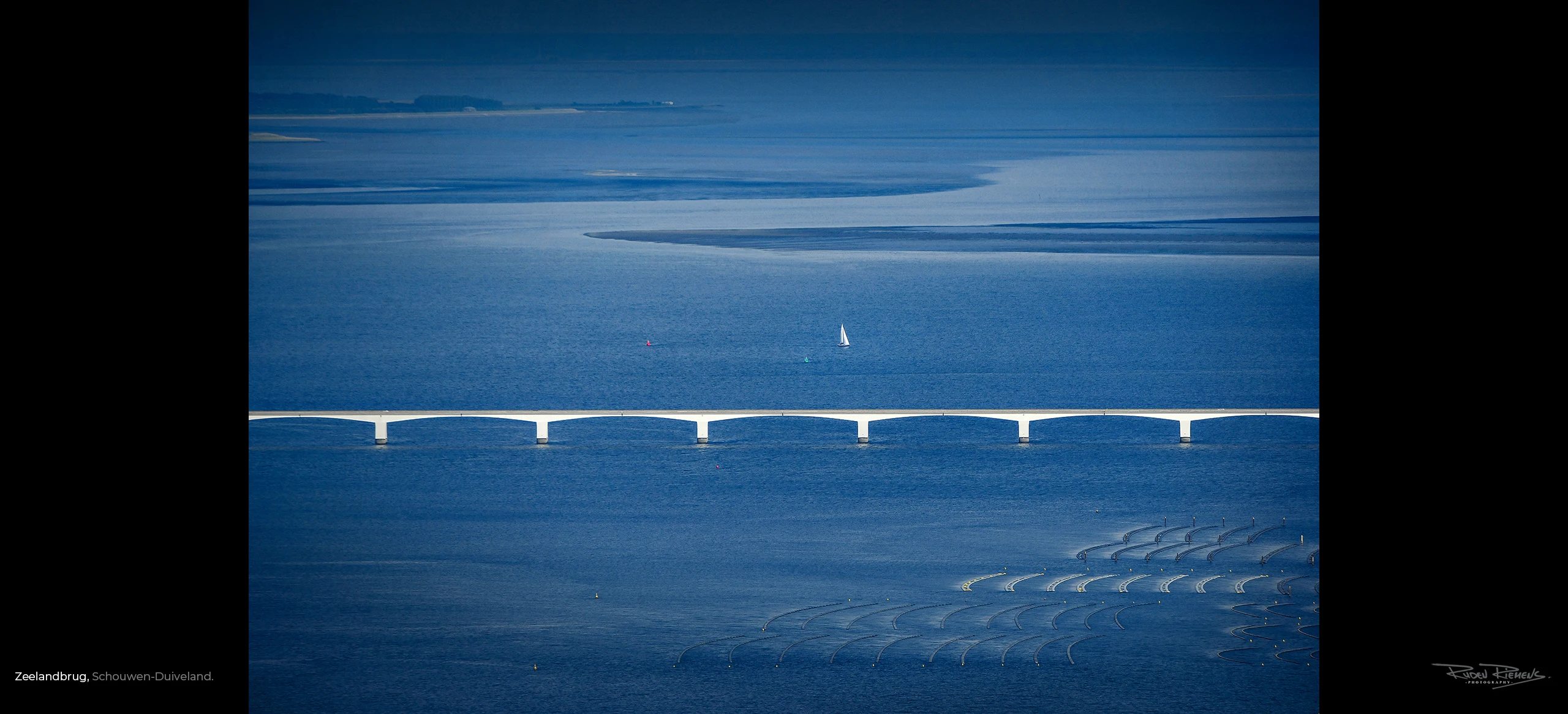 Een foto vanuit de lucht van de Oosterschelde met Zeelandbrug en zeilboot, gemaakt door Ruden Riemens fotograaf.