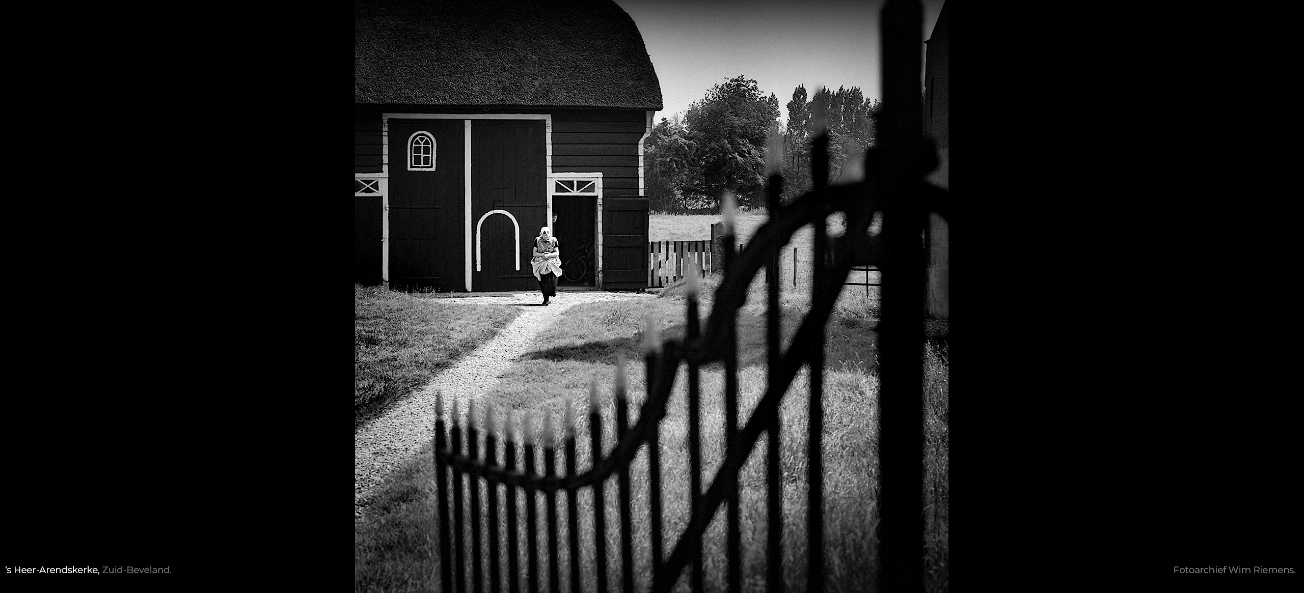 Wim Riemens fotografeerde dit mooie tafereel, boerin in Zeeuwse klederdracht op boerenerf met hek te 's Heer-Arendskerke in Zuid-Beveland.